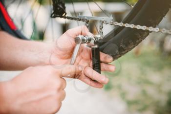 Bicycle mechanic  hands adjusts bike chain with service tools. Cycle workshop outdoor. Bicycling sport, bearded repairman
