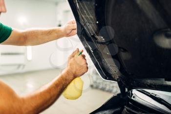 Man disperses soapy water on hood closeup. Protect car details against chips and scratches. Paint protection film. Protective coating