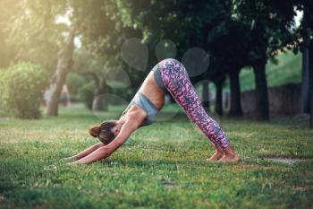 Woman doing yoga exercise, training on the grass in summer park. Morning yogi meditation