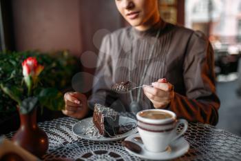 Woman eating delicious chocolate cake in cafe. Delicious dessert and cup of coffee close up shot. Woman sits at table in cafe, selective focus.