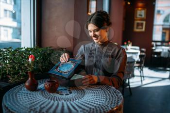 Young happy woman in cafe with casket and jewelry. Portrait of beautiful young retro lady with beads in her hands. Smiling brunette in vintage dress sitting in cafe.