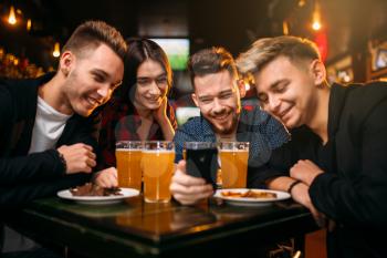 Fun company watches photo on phone in a sport bar, happy football fans