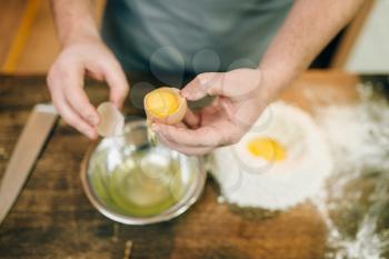 Pasta cooking process, male chef hands with egg, a bunch of flour on wooden table