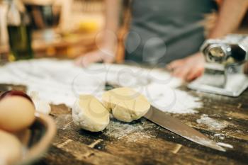 Male chef in apron, flour, dough, eggs and pasta machine on wooden table. Ingredients for homemade spaghetti cooking