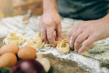 Male chef hands preparing fresh pasta on wooden kitchen table. Fettuccine preparation process
