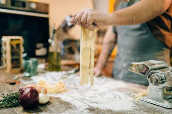 Chef with knife in hand cooking fresh homemade fettuccine in pasta machine on wooden kitchen table