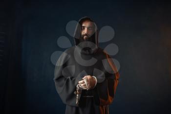 Medieval monk holds wooden cross in hands and praying, religion. Mysterious friar in dark cape. Mystery and spirituality