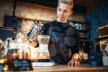 Young male barista makes latte, cafe counter and espresso machine on background. Barman works in cafeteria, bartender prepares coffee