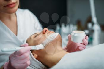 Doctor in gloves rubs the cream on female patient face, cosmetology clinic. Facial skincare, rejuvenation procedure in spa salon