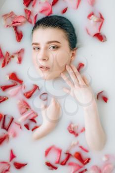 Young woman face in the bath with foam and rose petals. Full relaxation, romantic setting in bathroom