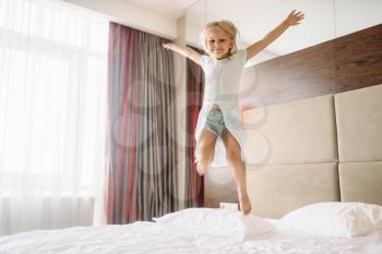 Little girl jumping on the bed in bedroom at home. A truly carefree childhood, happy time
