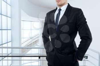 Businessman in tie and black suit poses in business center with glass walls