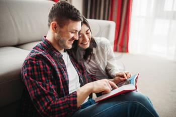 Happy love couple sitting on the floor and looks at the book together. Modern apartment interior of living room on background