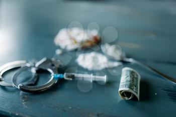 Junky kit, narcotics concept, addiction problem. Pills are laid out on wooden table, syringe for dose, alcohol and handcuff, top view