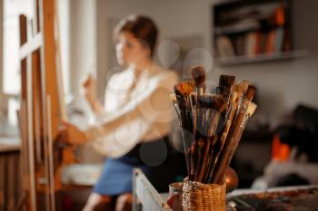 Brushes collection, female artist works at the easel in studio on background. Creative paint, painter drawing portrait in workshop