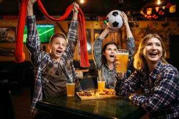 Football fans with scarf and ball in hands watching match and drinks beer in sports bar. Tv broadcasting, young friends leisures in pub, favorite team wins