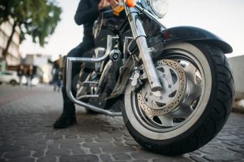 Biker in leather clothes poses on a motorcycle, front view from ground, classical chopper. Vintage bike, freedom lifestyle, biking