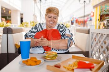 Fat woman prepares to eats fastfood in mall food court. Overweight female person at the table with junk lunch
