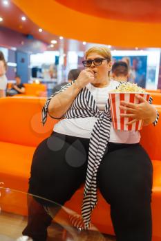 Fat woman holding popcorn in the cinema hall, unhealthy junk food. Overweight female person in mall, obesity problem