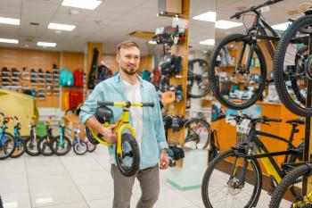 Young father with children's bicycle, shopping in sports shop. Summer season extreme lifestyle, active leisure store, customer buying cycle for family riding