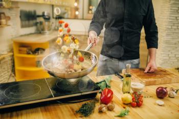 Male chef cooking meat with vetables into the frying pan on the kitchen. Man preparing beef on table electric stove