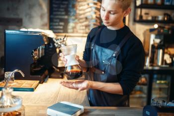 Young male barista makes fresh espresso at cafe counter. Barman works in cafeteria, bartender prepares black coffee