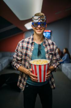 Male spectator in 3d glasses holds popcorn in cinema hall before the showtime. Man in movie theater, entertainment