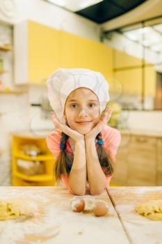 Little girl cook in cap and apron holds whisk for mixing, cookies preparation on the kitchen. Kids cooking pastry, children chefs preparing cake