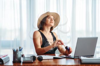 Young woman works on laptop at the table in office and dreaming about a vacation