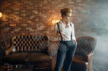 Woman in shirt and trousers with suspenders holding newspaper, retro fashion, gangster style. Vintage business lady in office with brick walls