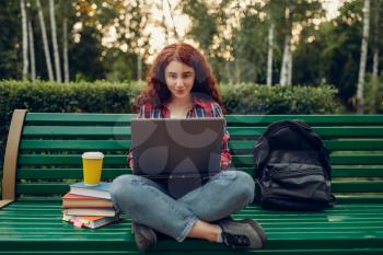 Female student with laptop sitting on the bench in yoga pose, summer park, front view. Ginger teenager leisures outdoors, pretty girl relax outside