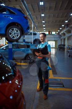 Worker with a checklist stands at vehicle with opened hood, car service station. Automobile checking and inspection, professional diagnostics