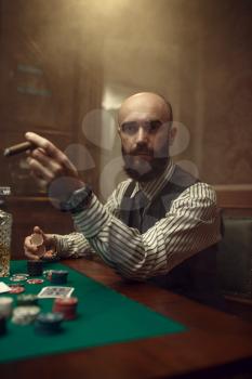 Bearded poker player with cigar playing in casino. Games of chance addiction. Man leisures in gambling house
