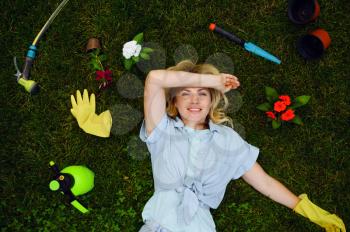 Young woman lying on the grass in the garden among gardening tools , top view. Female gardener takes care of plants outdoor, gardening hobby, florist lifestyle and leisure