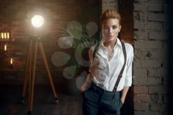 Business woman in strict clothes poses at the window in studio, retro fashion, gangster style. Vintage lady in office with brick walls