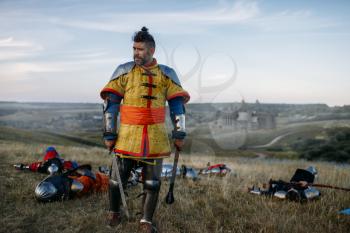 Old medieval knight in armor looks at the dead after great battle. Armored ancient warrior in armour posing in the field
