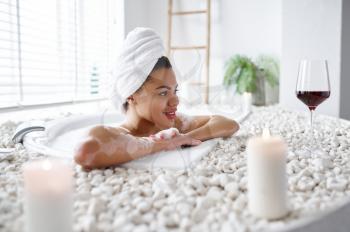 Smiling young woman relax in a bubble bath. Female person in bathtub, beauty and health care in spa, wellness treathment in bathroom, pebbles and candles on background
