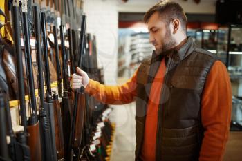 Man choosing rifle at showcase in gun shop. Euqipment for hunters on stand in weapon store, hunting and sport shooting hobby