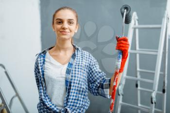 Female house painter with paint roller sitting on a ladder. Home repair, happy woman doing appartment renovation