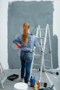 Female house painter looking on wall, back view. Home repair, happy woman doing appartment renovation, room decoration renovating