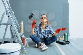 Indignant female house painter with paint roller sitting on the floor after work. Home repair, happy woman doing appartment renovation