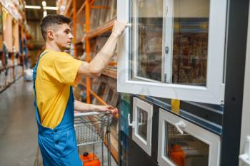 Male constructor choosing windows in hardware store. Builder in uniform look at the goods in diy shop