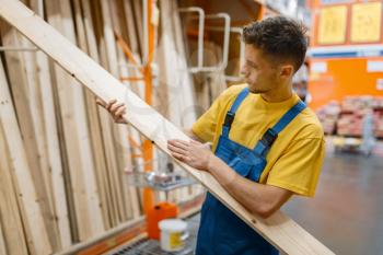 Male constructor choosing wooden boards in hardware store. Builder in uniform look at the goods in diy shop