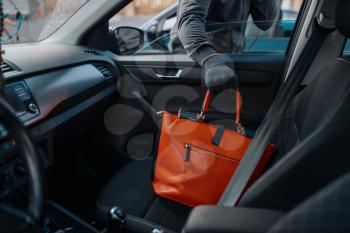 Car robber steals women's handbag, criminal lifestyle, stealing. Hooded male bandit opening vehicle on parking. Auto robbery, automobile crime