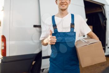 Deliveryman in uniform holding parcel and shows thumbs up, and notebook, carton boxes in the car, delivery. Man standing at cardboard packages in vehicle, male deliver, courier or shipping job