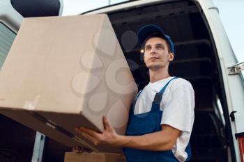 Loader in uniform holding carton box, delivery service. Man standing at cardboard packages in vehicle, male deliver, courier or shipping job