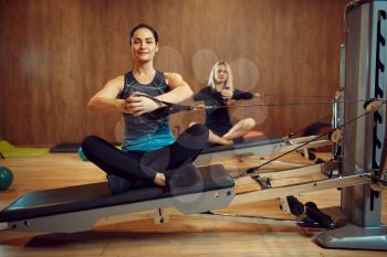 Two women on pilates training on exercise machine in gym, flexibility. Fitness workuot in sport club. Athletic female person, aerobics indoor, body stretching