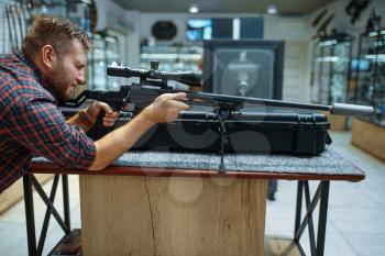 Man aims with sniper rifle in gun shop. Euqipment for hunters on stand in weapon store, hunting and sport shooting hobby
