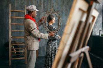Portrait painter holds frame, female model in art studio. Male artist standing at his workplace, creative master in workshop