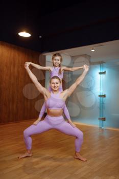 Mother and daughter, balance exercise in gym, yoga workout. Mom and little girl in sportswear, woman with kid on joint training in sport club
